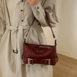 Detail of dark burgundy leather underarm bag with silver buckles and a metal plaque