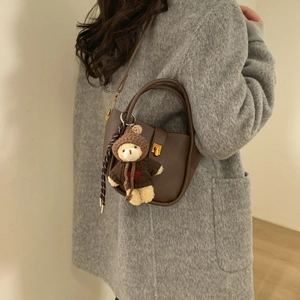 Brown lychee leather bucket bag with gold clasp and cute teddy bear charm on grey coat