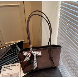 Détail rapproché d'un sac cabas tressé marron foncé avec foulard en soie et anses en cuir