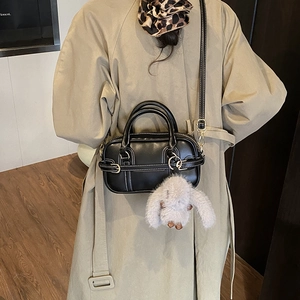 Detail of black retro pillow bag with white stitching and plush bunny pendant on model