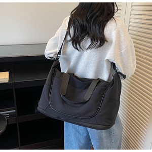 Rear view of a model carrying a large black nylon travel bag with shoulder strap
