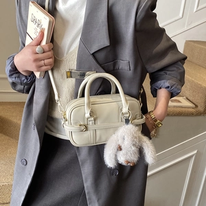 Detail of a beige pillow handbag with a cute white rabbit plush charm and golden hardware