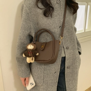 Close-up of brown pebbled leather bucket bag with gold clasp and plush bear charm