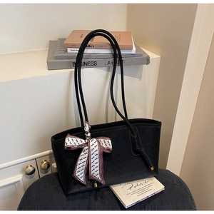 Détail d'un cabas noir tressé avec foulard en soie sur un coussin en cuir chic