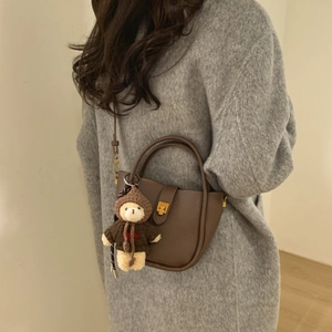 Detail of dark brown pebbled leather bucket bag with T-shaped clasp and bear charm