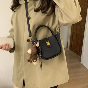 Detail of black pebbled leather bucket bag with gold clasp and plush bear charm