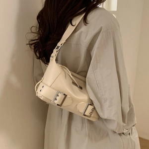 Detail view of cream underarm bag with decorative metal buckles on polished leather
