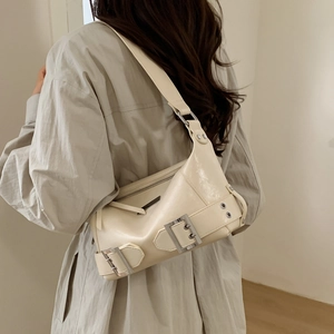 Detail of cream glossy patent leather shoulder bag with silver buckle straps and sleek finish