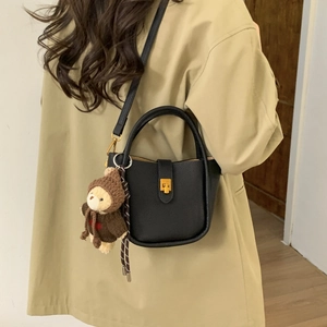 Detail of black pebbled leather bucket bag with gold twist lock and bear plush charm