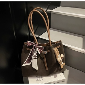 Close-up of brown suede tote bag featuring silk scarf bow and plush animal charm detail