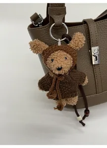 Dettaglio di un orsetto di peluche appeso a una borsa a secchiello marrone martellata