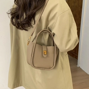 Detailed close-up of beige lychee grain leather texture and gold buckle on shoulder bag