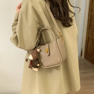 Detail of khaki litchi leather bucket bag with gold lock and cute bear plush charm