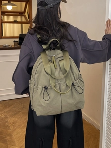 Army green nylon backpack with drawstring side pockets worn by a model in a room