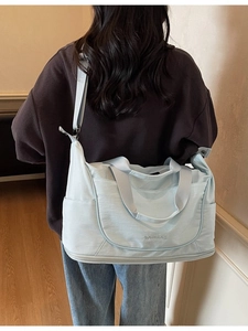 Light blue large capacity travel bag worn crossbody by a model in a home setting