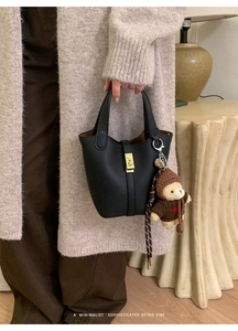 Gros plan du sac seau noir en cuir grainé avec fermoir doré et pendentif ourson