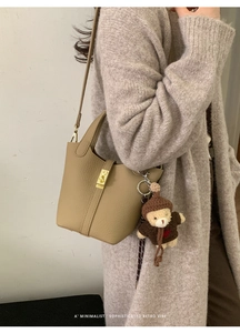 Détail du sac seau en cuir kaki avec texture grainée et un charmant ours en peluche