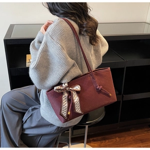 Détail du sac cabas bordeaux tressé orné d'un nœud en foulard de soie sur la sangle