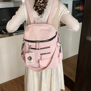Detailed view of pink multi-pocket nylon backpack with decorative charm and zippers
