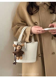 Dettaglio borsa a secchiello in pelle bianca con ciondolo orsetto su cappotto di lana