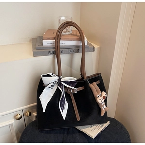 Detail of a black tote bag featuring a leather handle, silk scarf, and cute bear charm