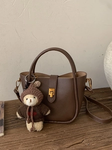 Retro brown leather bucket bag with top handle and cute bear charm on a wooden table