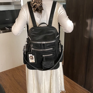 Detail of a black multi-zipper backpack with soft texture and cartoon dog charm accessory