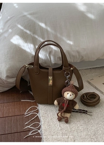 Détail d'un sac seau en cuir marron avec un petit ours en peluche sur un tapis blanc