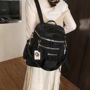 Detail of a black multi-pocket travel backpack with silver zippers and a cute card charm
