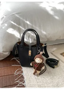 Détail du sac seau en cuir grainé noir avec charme d'ours sur un tapis blanc