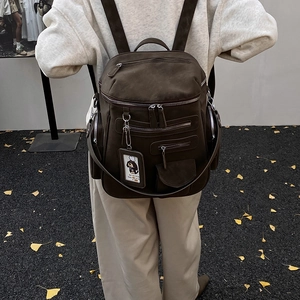 Close-up of vintage brown suede multi-pocket backpack with dog charm on autumn ground