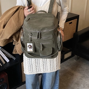 Detail view of olive green suede backpack featuring multiple metal zippers and front flap pocket
