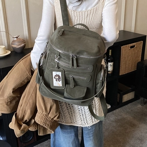 Detail of army green multi-pocket backpack showing functional zippers and cute charm