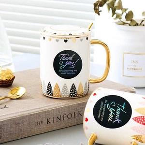 Black round small business thank you stickers with gold foil lettering on a white ceramic mug