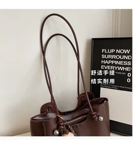 Detail of dark brown tote bag with leather texture, knotted strap and fuzzy ball charm