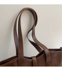 Detail view of long shoulder straps and reinforced stitching on a brown leather tote bag