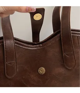 Macro detail of the golden magnetic buckle and stitching on a brown leather tote bag