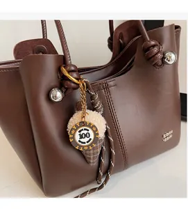 Close-up of a brown leather tote bag featuring a plush ice cream charm and metal hardware detail
