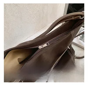 Detail of silver zipper hardware and white contrast stitching on dark brown suede tote bag