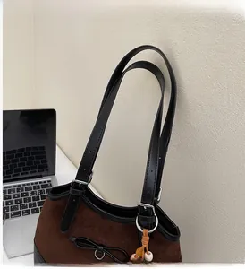 Detail of suede tote bag with leather straps, metallic buckle, and decorative bow
