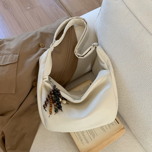 Close-up of beige lychee texture bag on a sofa with wooden bead tassel and book