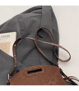 Détail du sac bandoulière en daim marron avec œillets argentés et pompon sur blazer gris