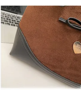 Close-up of heart charm on brown suede and black leather shoulder bag with fine stitching