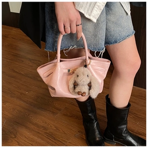 Détail d'un sac à main plissé rose clair avec breloque lapin et boucle en métal