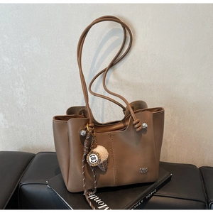 Detail of brown tote bag with metal logo and ice cream charm on stacked books