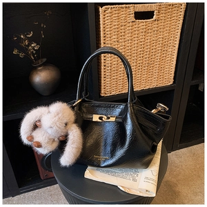 Détail d'un sac plissé noir en simili cuir avec un charme de lapin en peluche beige