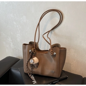 Detail of brown leather tote bag with metal logo and plush ice cream charm accessory