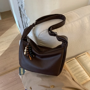 Detail of dark brown pebbled leather shoulder bag with ethnic wooden bead charm