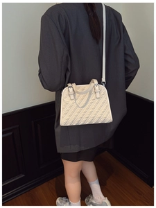 Detalle de bolso bandolera blanco trenzado con silueta de concha sobre blazer oscuro