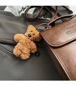 Detail of brown teddy bear charm on textured faux leather flap bag with embossed logo